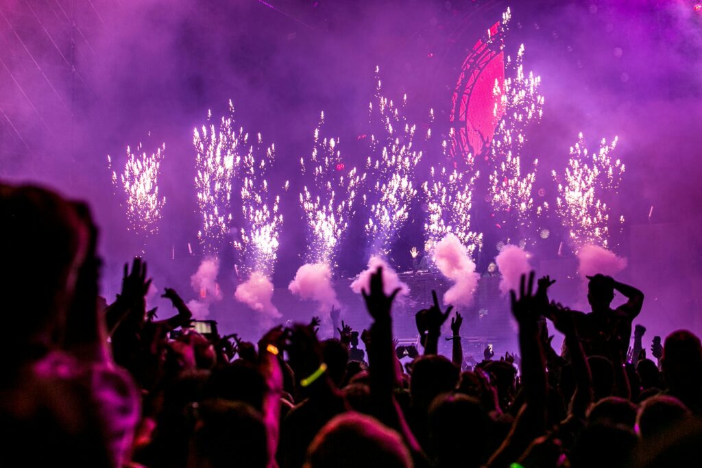 Publikum fester foran scene med DJ, røg, lys og fyrværkeri i lilla nuancer – DJ Gram tilbyder professionel DJ-service med lys- og lydeffekter til private events, firmafester og større arrangementer i hele Danmark.