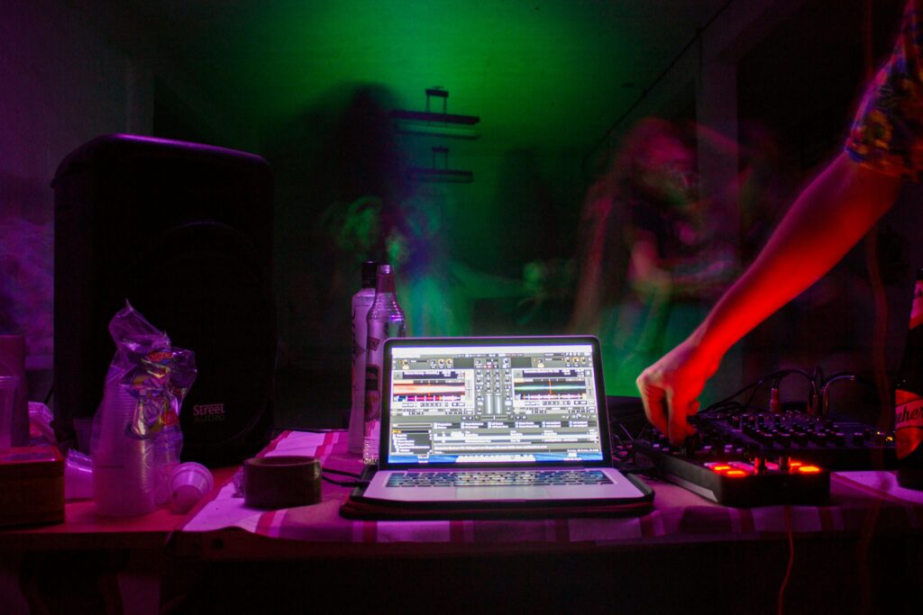 DJ-setup med laptop, mixerpult, højtaler og festlys i lilla og grønne nuancer – DJ Gram tilbyder mobil DJ-service til private events, ungdomsfester, fødselsdage og firmafester i hele Danmark.