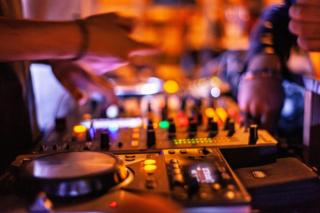 Nærbillede af DJ-hænder, der styrer mixerpult med farverige knapper og lys – DJ Gram tilbyder professionel DJ-service til private events, ungdomsfester, fødselsdage og firmaarrangementer i hele Danmark.