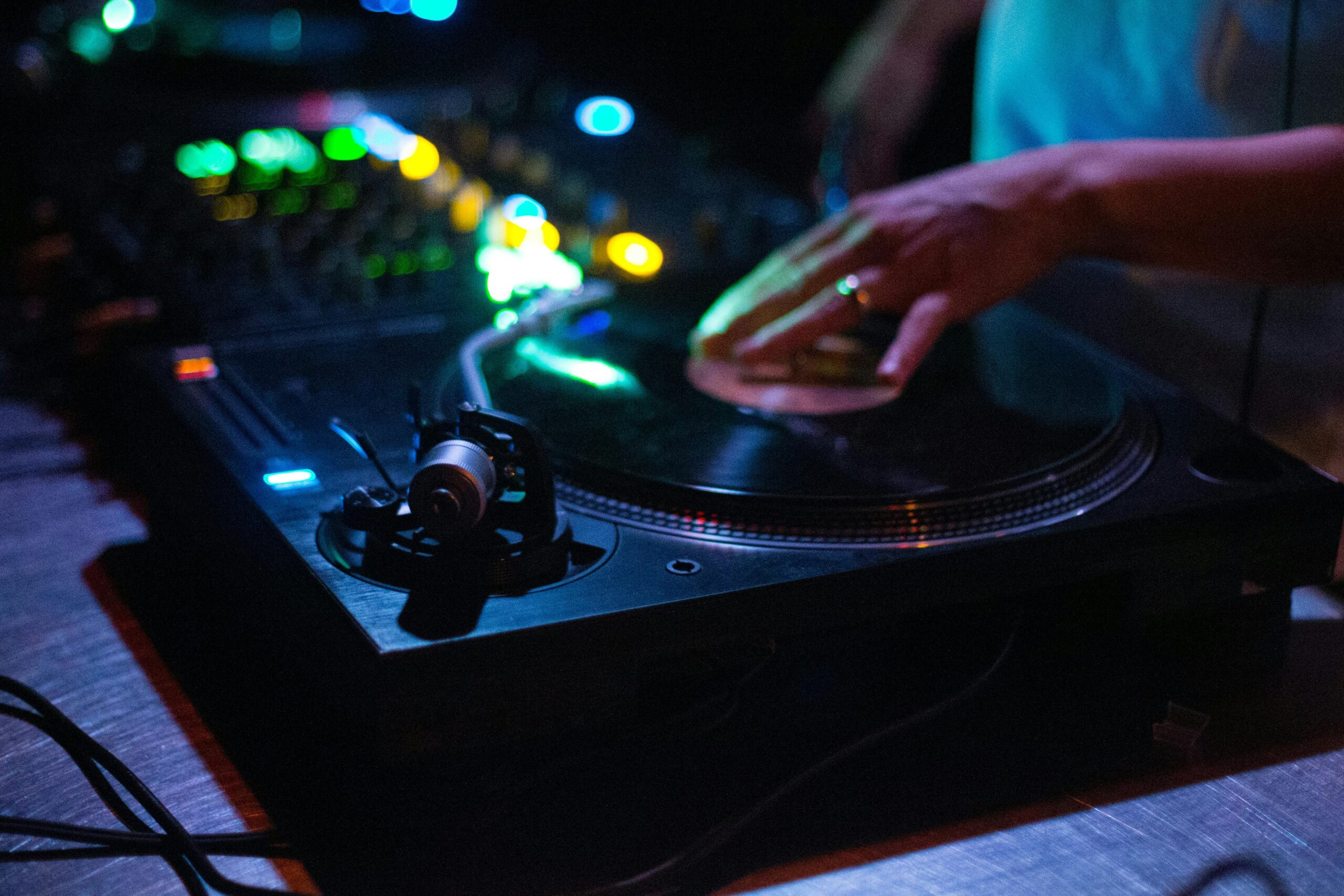 Nærbillede af DJ-hånd, der betjener en mixerpult med lys og vinylplade – DJ Gram tilbyder professionel DJ-service til private events, bryllupper, firmafester og fødselsdage i hele Danmark.
