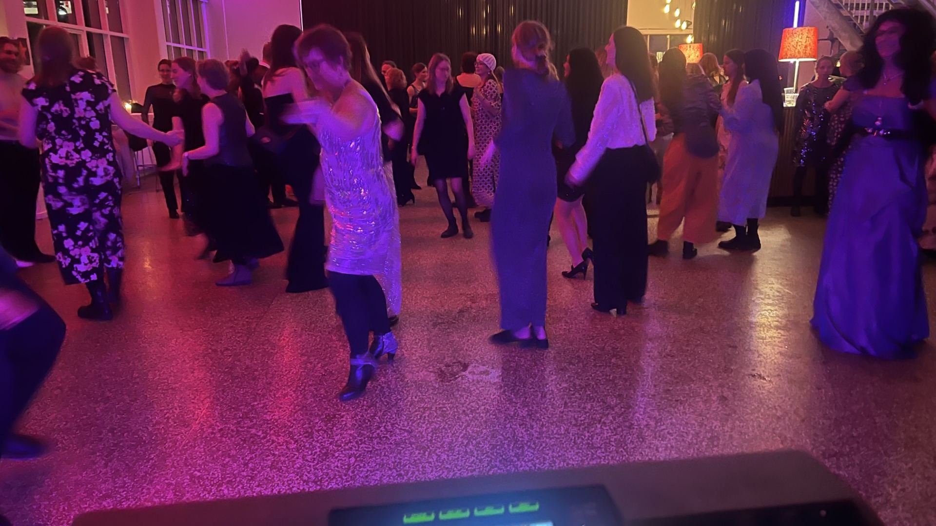 Large crowd of well-dressed guests dancing at indoor event space with magenta and purple ambient lighting, polished floor, contemporary décor and designer details