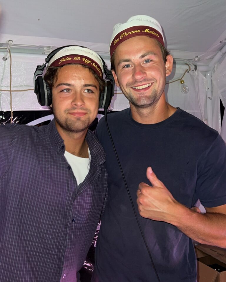 Two DJs posing inside tent wearing matching headbands, one with headphones on, both smiling and giving thumbs up during event
